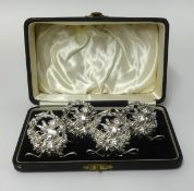 A set of four silver place setting holders in fitted case each decorated with a winged cherub,