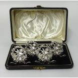 A set of four silver place setting holders in fitted case each decorated with a winged cherub,