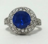A modern silver dress ring set with blue stone and diamond effect cluster.