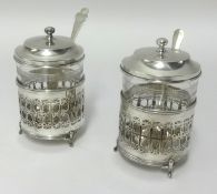 A pair of George V silver and glass jam pots, maker E.S.B, with spoons (not matching) height 11cm.