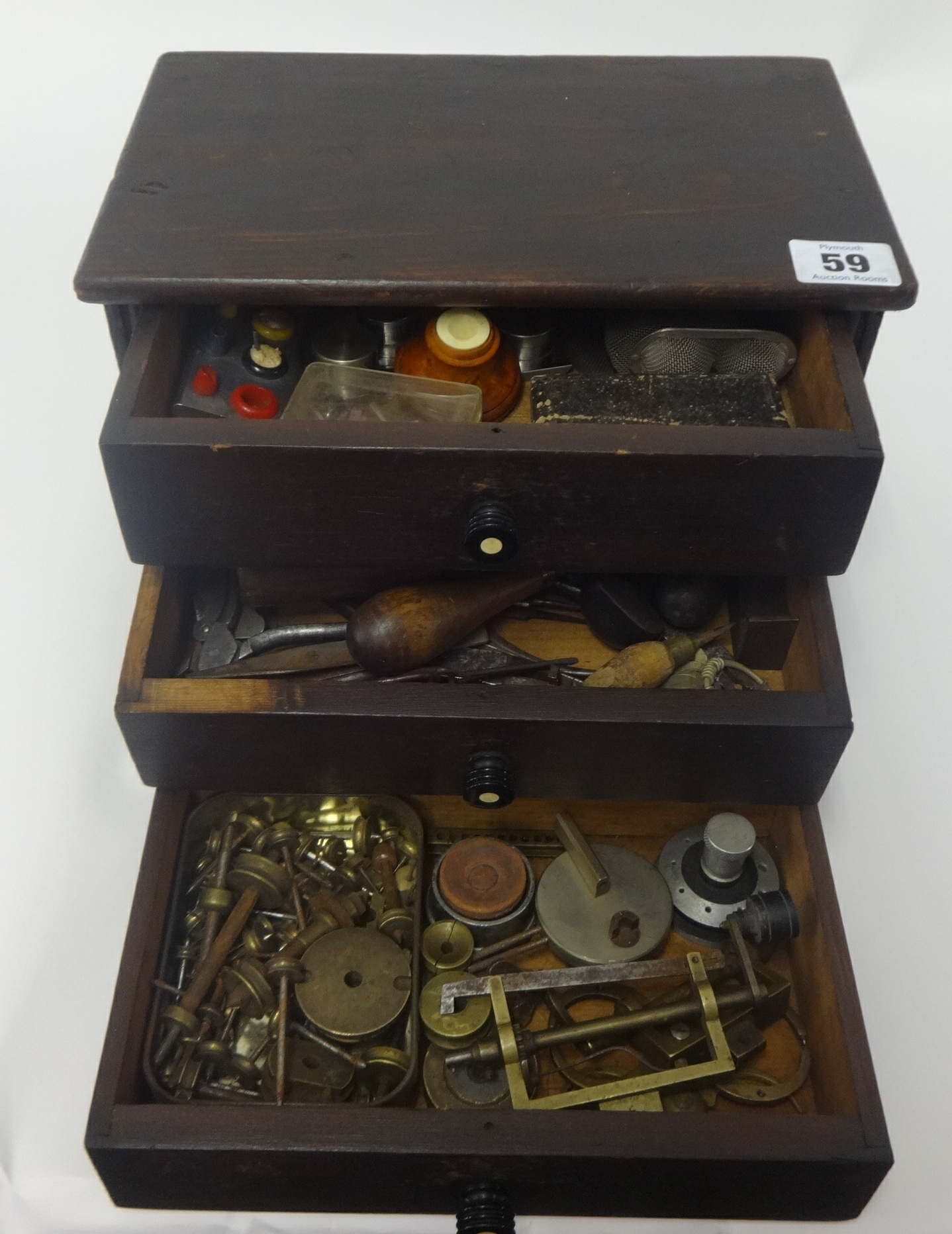 A small chest fitted with three drawers containing assorted watch parts, small tools, clamps etc.