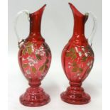 A pair of Victorian cranberry glass and enamelled ewers.