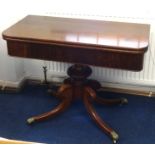 A Regency mahogany fold over card table on pedestal base with brass capped castors.