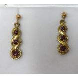 A pair of antique yellow metal drop earrings each set with three red stones, length 27mm.