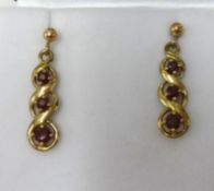 A pair of antique yellow metal drop earrings each set with three red stones, length 27mm.