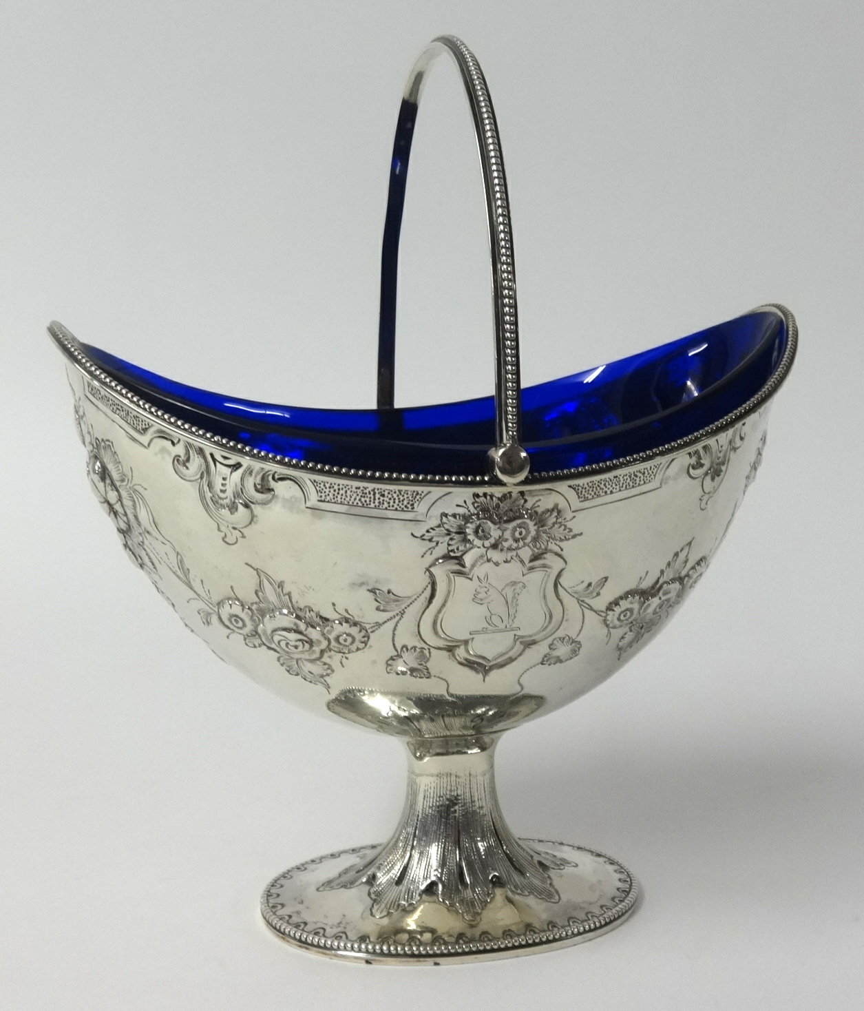 A Victorian silver sugar basket embossed with flowers, with swing handle and blue glass liner, maker