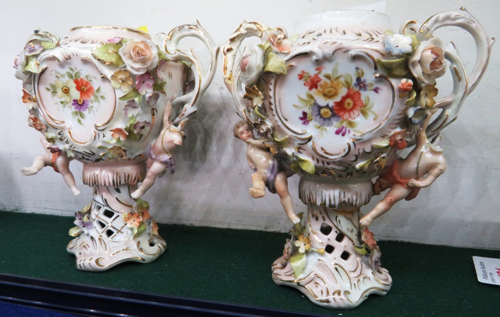 PAIR OF CONTINENTAL PORCELAIN URN SHAPED VASES ENCRUSTED WITH FLOWERS AND MOULDED WITH CHERUBS, WITH