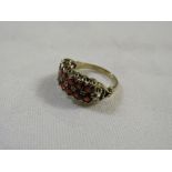 A yellow metal ring set with fourteen small garnets in two rows, scrolled and pierced at the