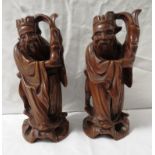 Pair of Chinese carved wooden figures depicting robed dignitaries holding objects aloft, each carved