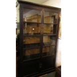 An early 20th century black lacquered Chinese style glazed two door shelving unit with typical