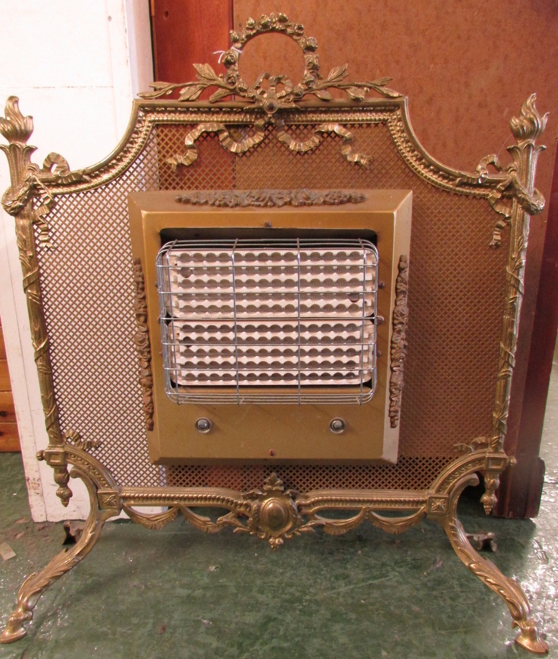 A vintage electric fire in a brass mesh frame standing on four hoof feet with acanthus mouldings,