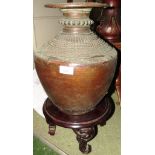 LARGE HAND BEATEN COPPER URN AND A CIRCULAR WOODEN STAND