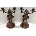 A pair of bronze figural table lamps modelled as putti holding aloft flower head nozzles, on oak