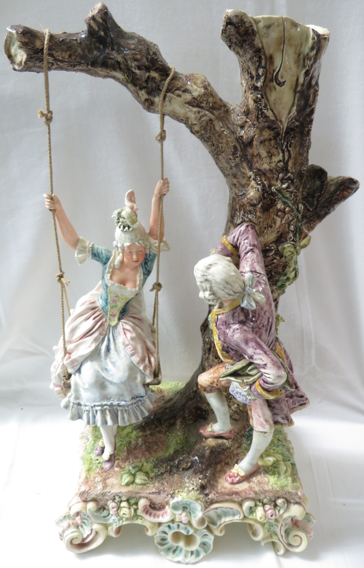 A large polychrome glazed pottery model of a lady in a swing seat suspended from a tree with