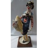 A Capodimonte resin figure of a clown reading a book held between his toes, signed G Armani with