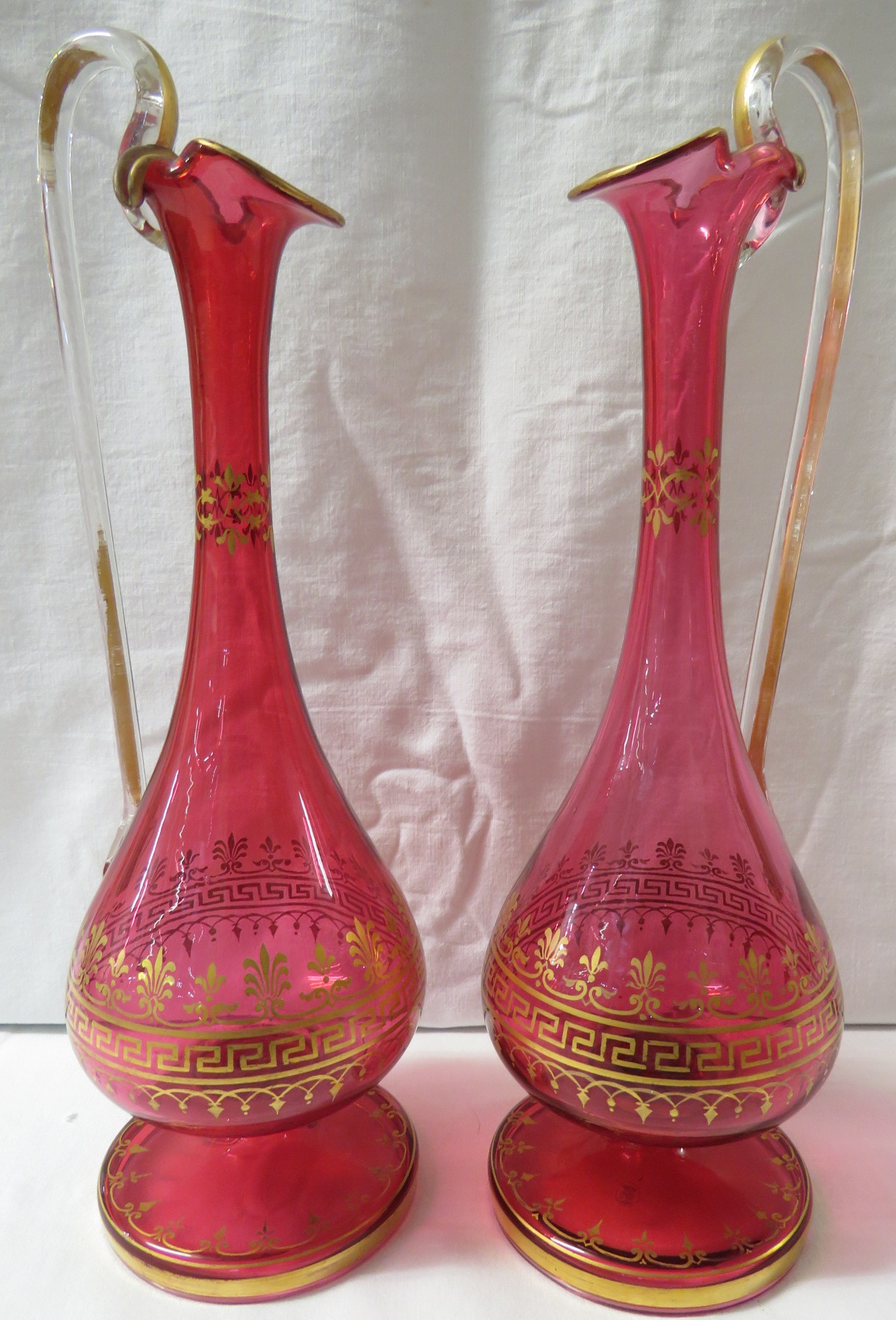 A pair of Victorian long stemmed cranberry glass ewers with key fret gilding, height 27cm