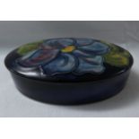 Moorcroft pottery oval lidded box, dark blue ground, the lid decorated with a blue flower, the