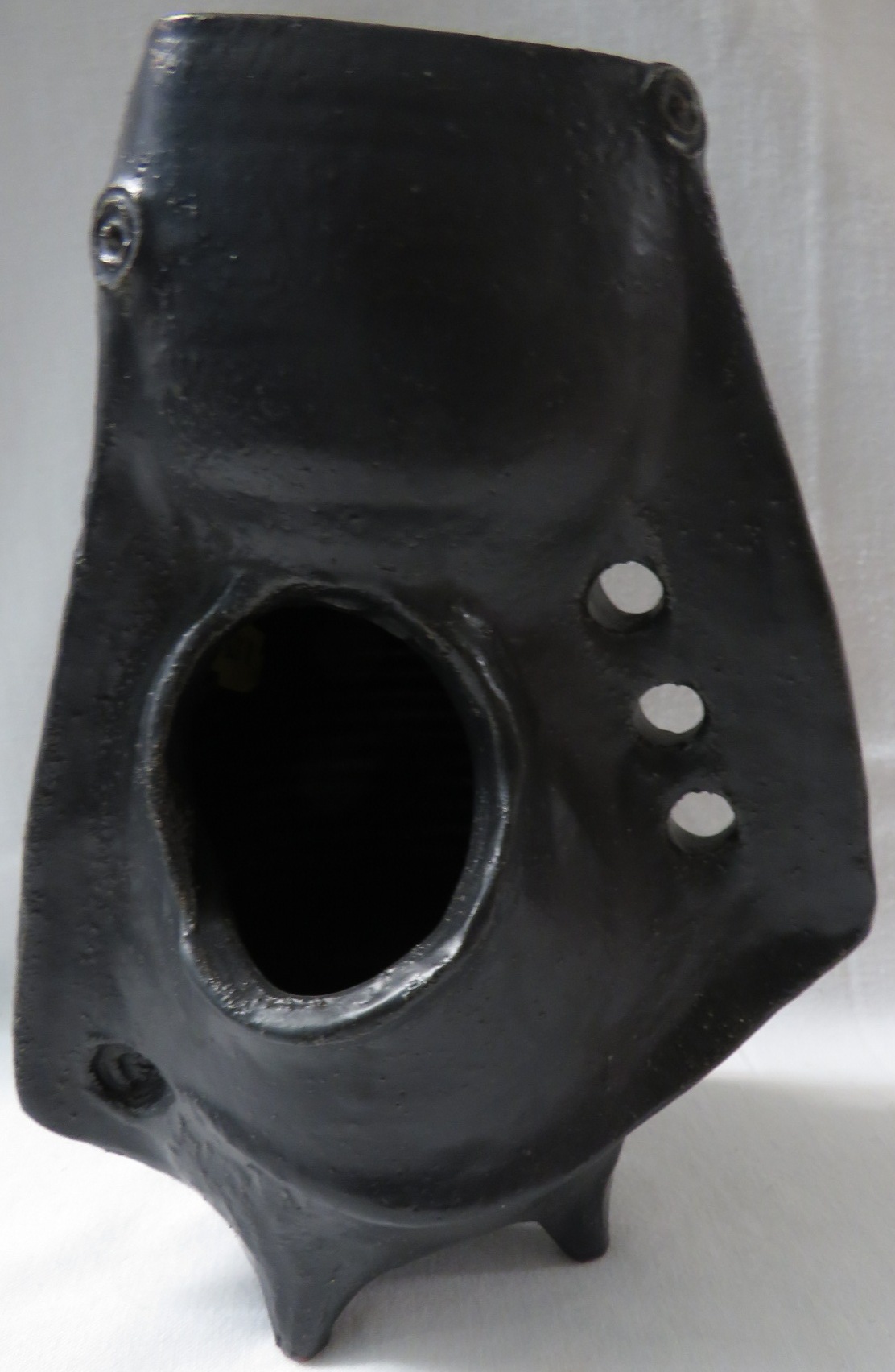 Pottery vase of abstract form in a black glaze with flanges and excised circles, standing on four