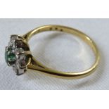 A cluster dress ring with a central green stone surrounded by eight small white stones which do