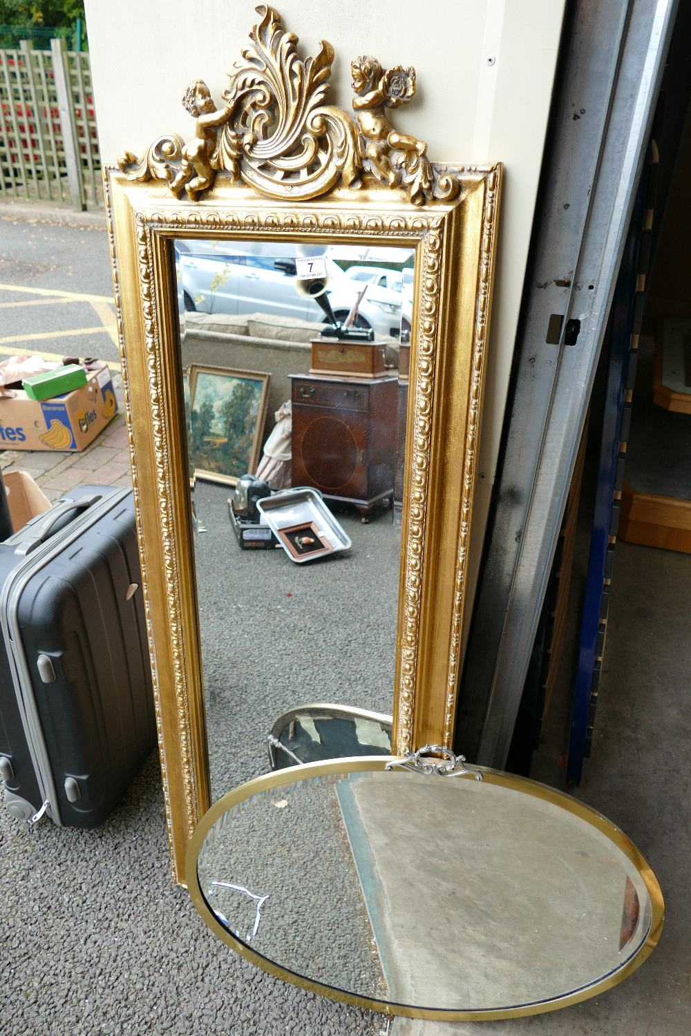 A reproduction rectangular gilt mirror with beval edge and cherub design with a similar oval mirror.