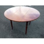 A circular pine dining table, the top from a drop-leaf, raised on turned tapering legs.