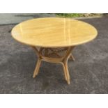 A circular dining table, the top supported on a cane base with round tray platform stretcher, the