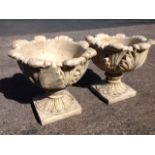 A pair of composition stone leaf moulded urns, the bowls on squat columns with square platform bases