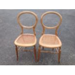 A pair of Victorian oak balloon back chairs, with cane seats, supported on turned legs & stretchers.