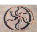 A large 3ft cast iron fly wheel, with six scrolled spokes, and outer rim with cog teeth.