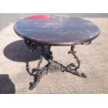 A circular garden table with hardwood top supported on scrolled cast iron base with three legs