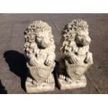 A pair of composition stone lions, seated on their haunches holding "welcome" shields, supported