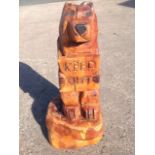A chainsaw carved bear, cut from a solid treetrunk, the animal holding Keep Out sign, on log base.