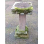 A carved sandstone birdbath , with square bowl on tapering column above a stepped plinth base.