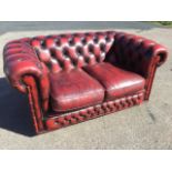 A two-seater leather sofa with padded button upholstered back and arms above loose cushions