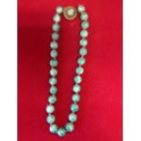 A jade bead necklace, with twenty nine hand-knotted varigated beads, fitted with circular brass