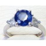 An 18ct gold sapphire & trillion cut diamond ring, the circular set sapphire of over two carats