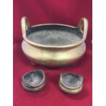 An oriental brass spittoon, the bulbous bowl on three feet, cast with loop handles -