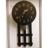 An arts & crafts ebonised oak wallclock, the circular dial with brass numerals and hands, above a