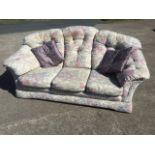A three-seater sofa with floral tapestry style button upholstery and loose cushions with padded