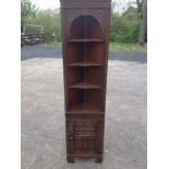 A carved oak corner cabinet with moulded cornice above an arched floral apron, with adjustable