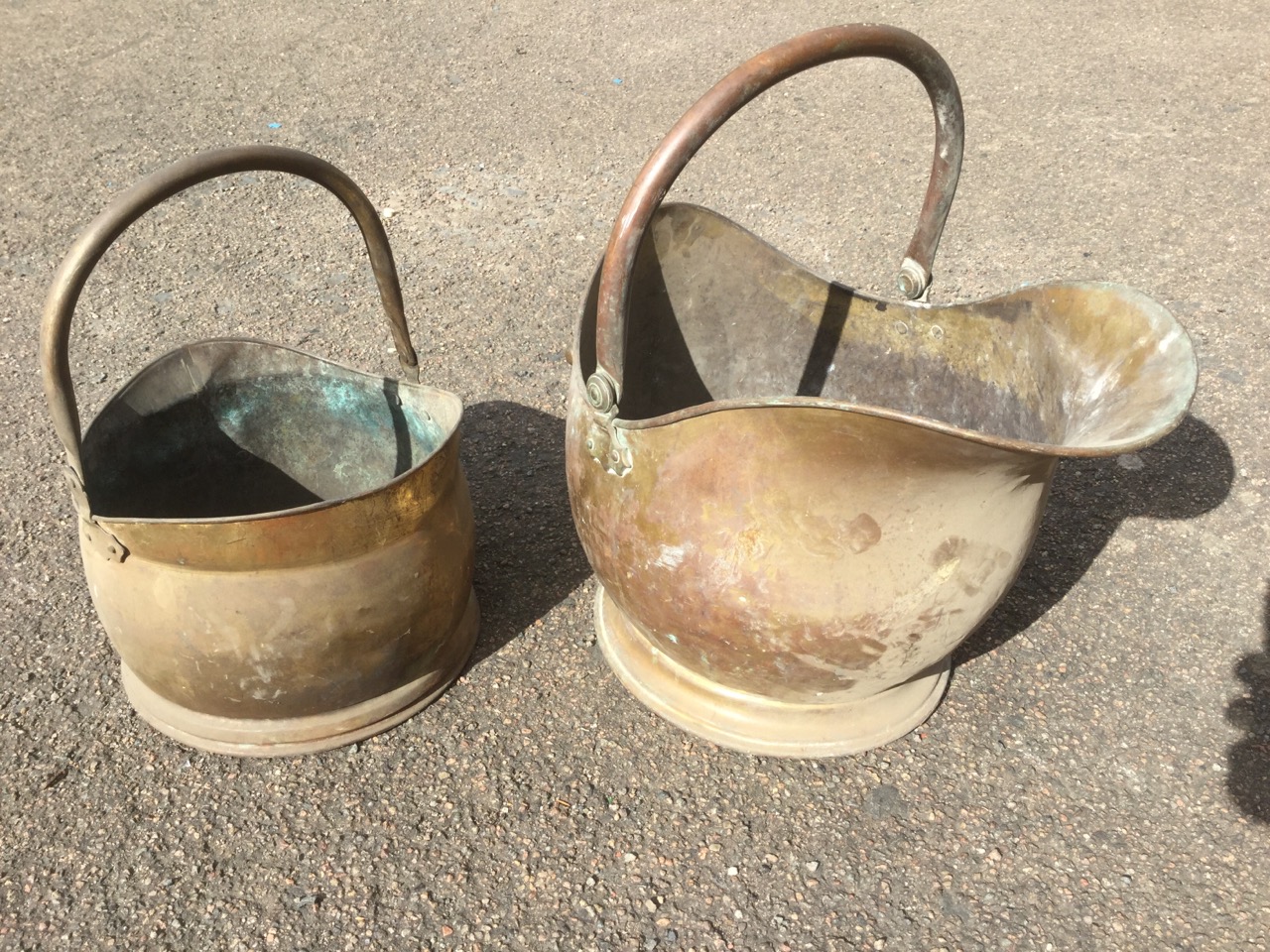 A brass helmet shaped coal skuttle with rolled rim and swing handle; and another similar smaller. (