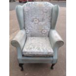 A wing back armchair with button upholstered back above loose cushion seat with padded arms,