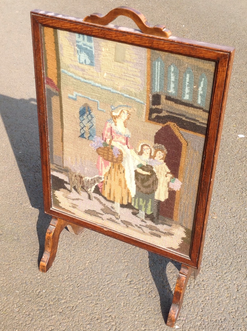 An oak framed firescreen, the woolwork tapestry panel depicting a mother with her children & dog.