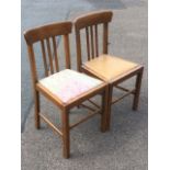 A pair of oak side chairs with lathe backs beneath shaped bar rails above drop-in upholstered seats,