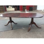 A Georgian style twin pedestal mahogany dining table, the extending top with two leaves supported on