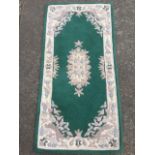 An Indian wool rug, woven with emerald green field and oval floral medallion, the spandrels of