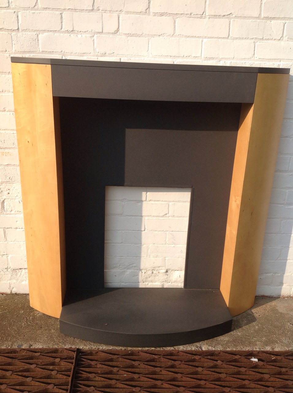 A contemporary chimneypiece in maple with graphite finish, the bowfronted hearth and indented