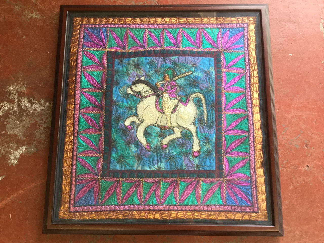 A large framed embroidered and quilted tapestry depicting a horse & rider, with leaf border.