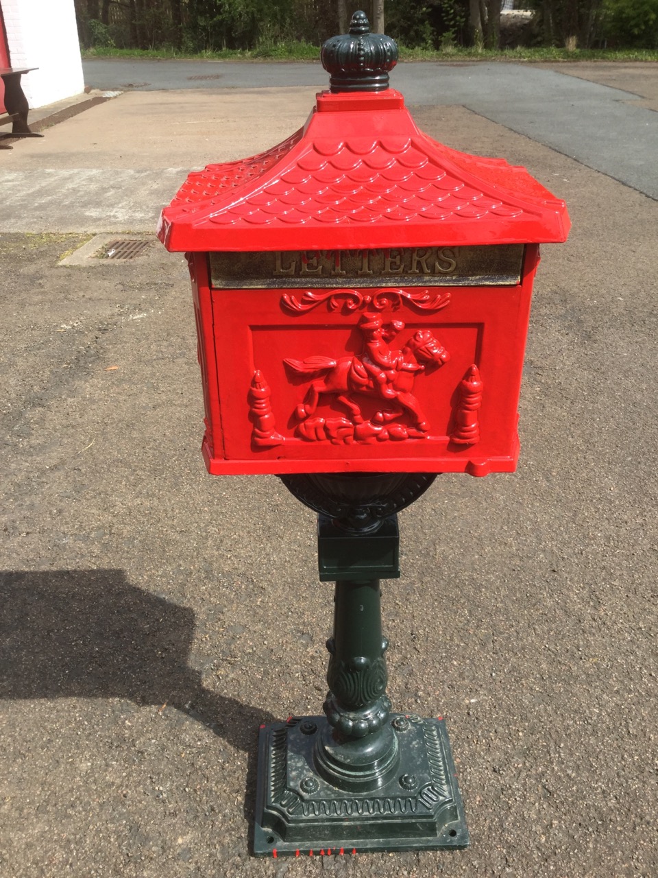 A metal postbox, the container with letterbox embossed with postboy & horn panels beneath a