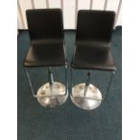 A pair of breakfast stools, the shaped padded seats with suspended tubular footrests, supported on